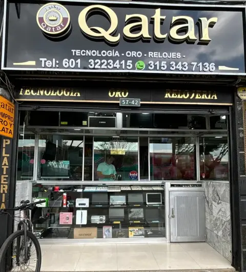 Fachada de Compra y Venta Qatar, con el aviso dorado y la vitrina iluminada
