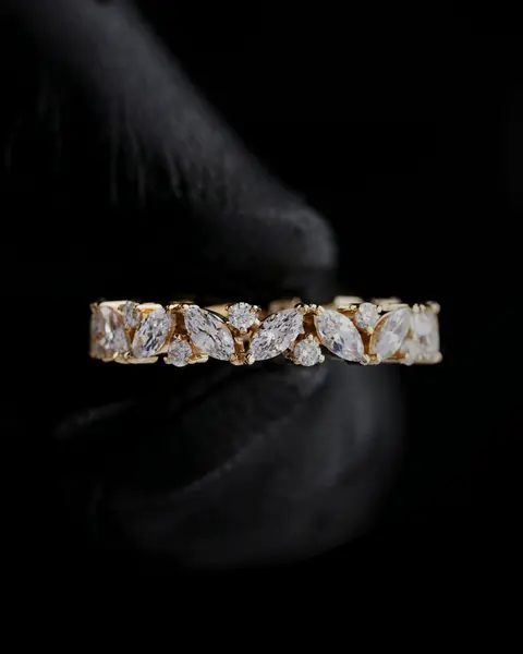 Anillo de oro con piedras claras sostenido por una mano con guante negro